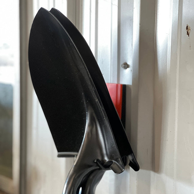 A black garden trowel is stored by hanging its handle on a red Gator Magnetics magnetic hook attached to a steel wall panel.