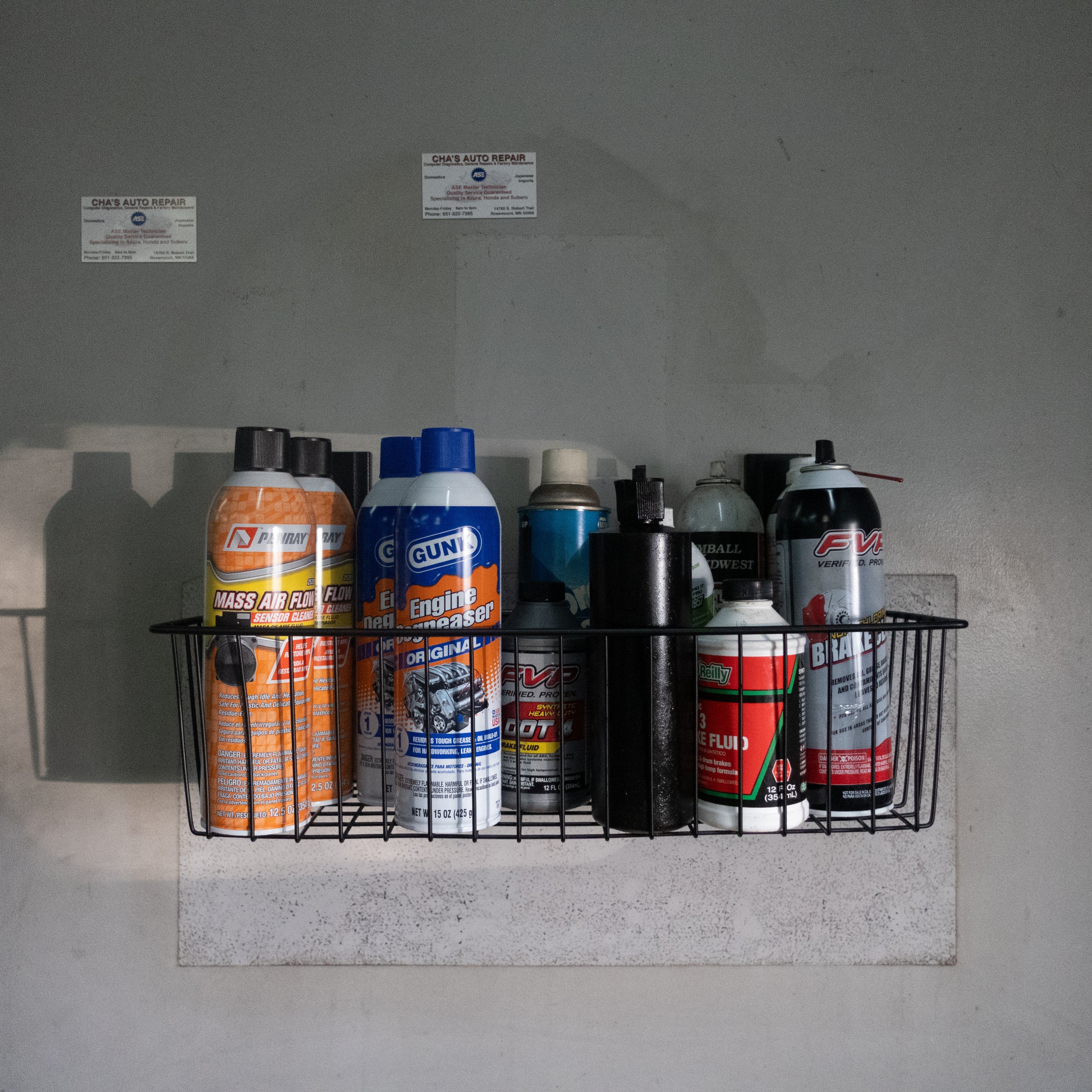 Black Gator magnetic storage basket on a steel wall panel holding automotive spray cans and bottles.
