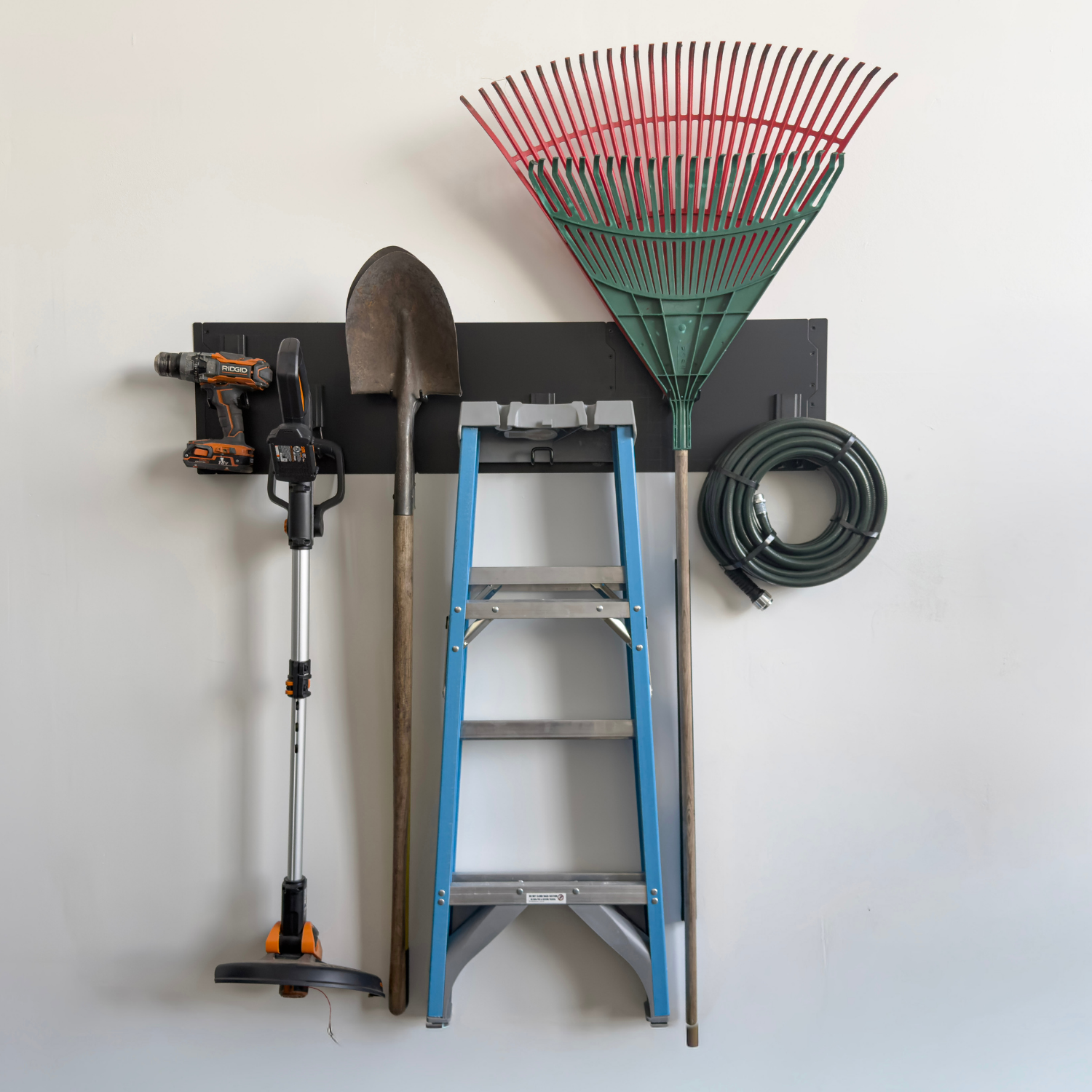 Black magnetic wall panels holding a ladder, rakes, power tools and a coiled hose.
