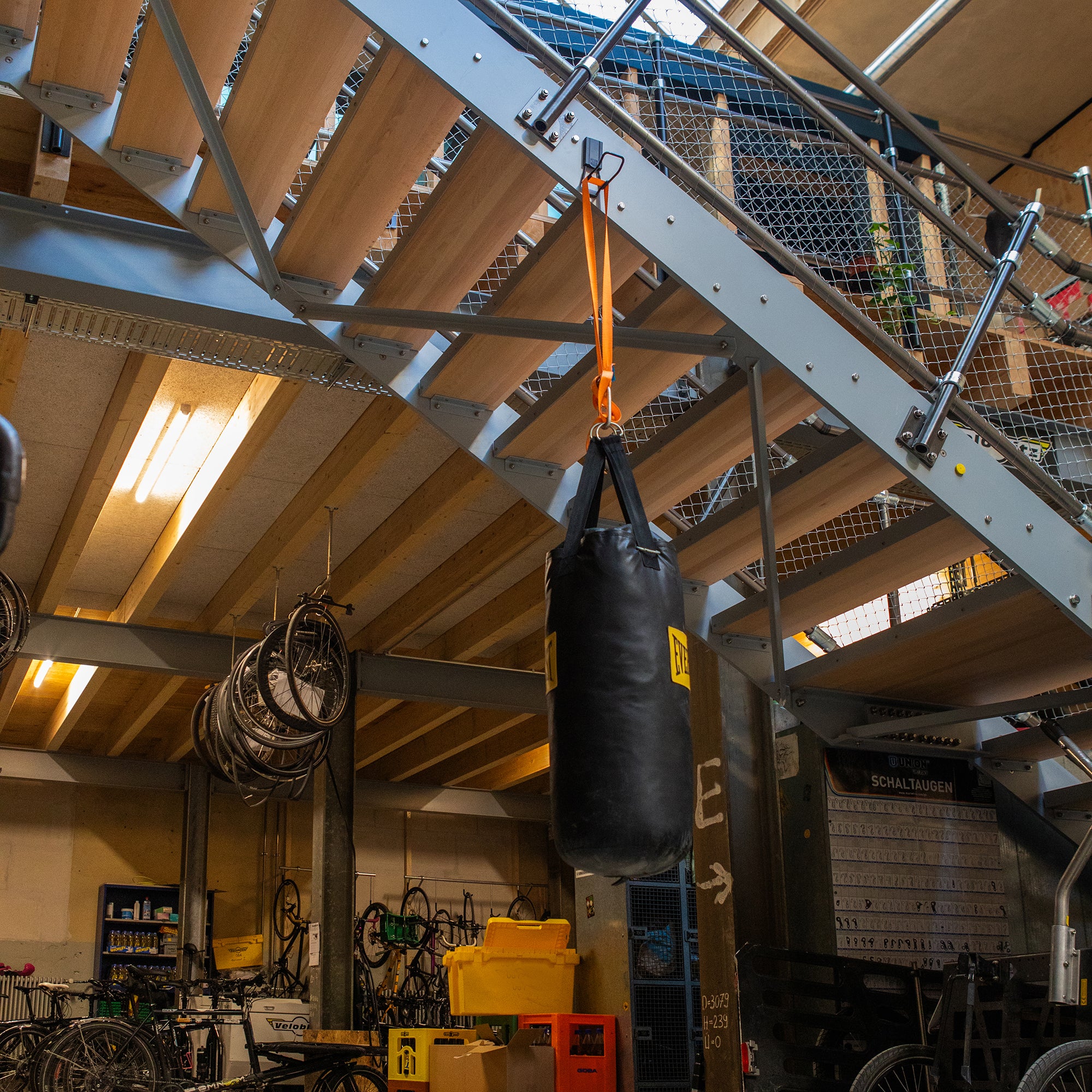 Black punching bag hanging from a Gator heavy-duty magnetic hook on a steel staircase beam.