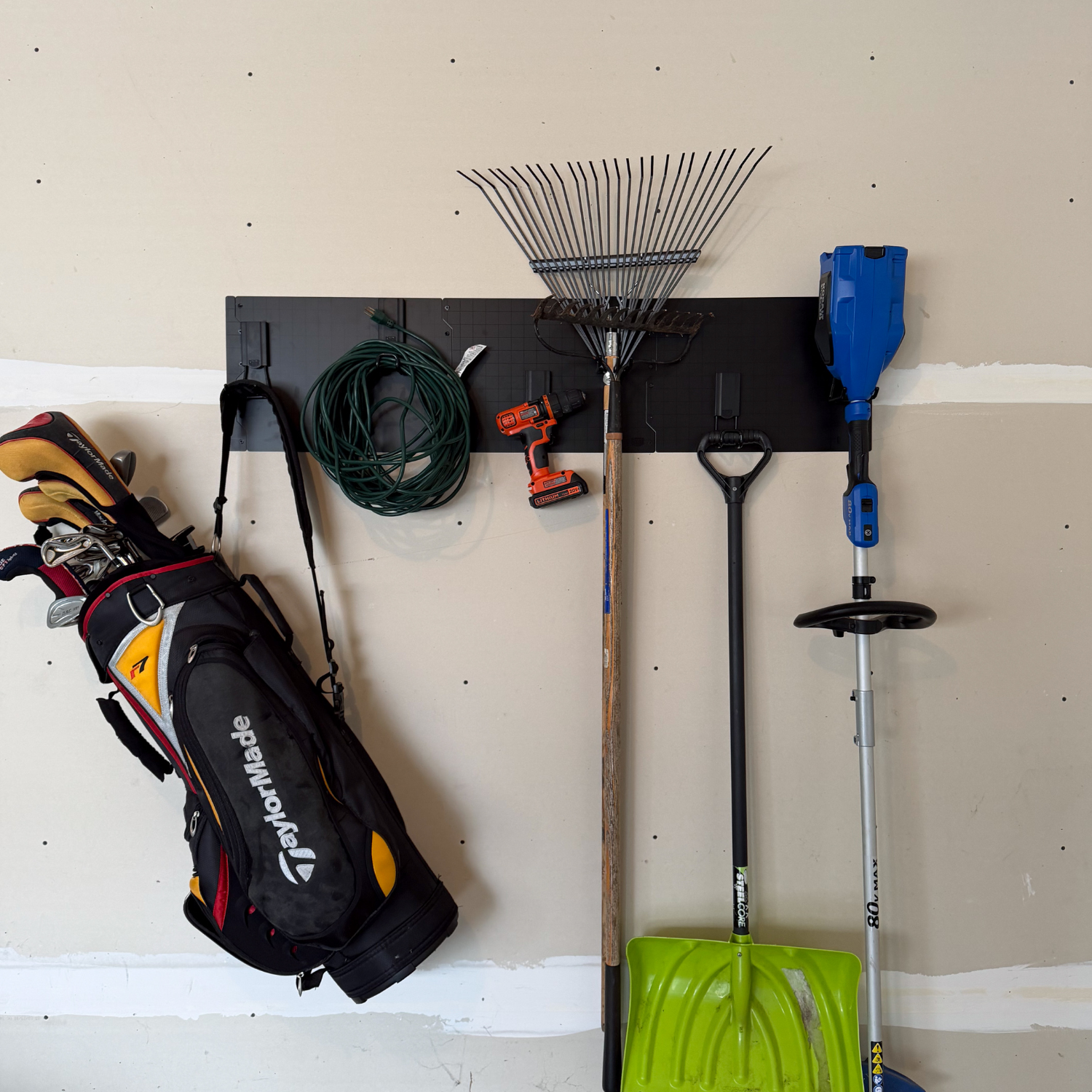 Black steel wall panels organizing golf bags, rakes, cords, a shovel and power tools.