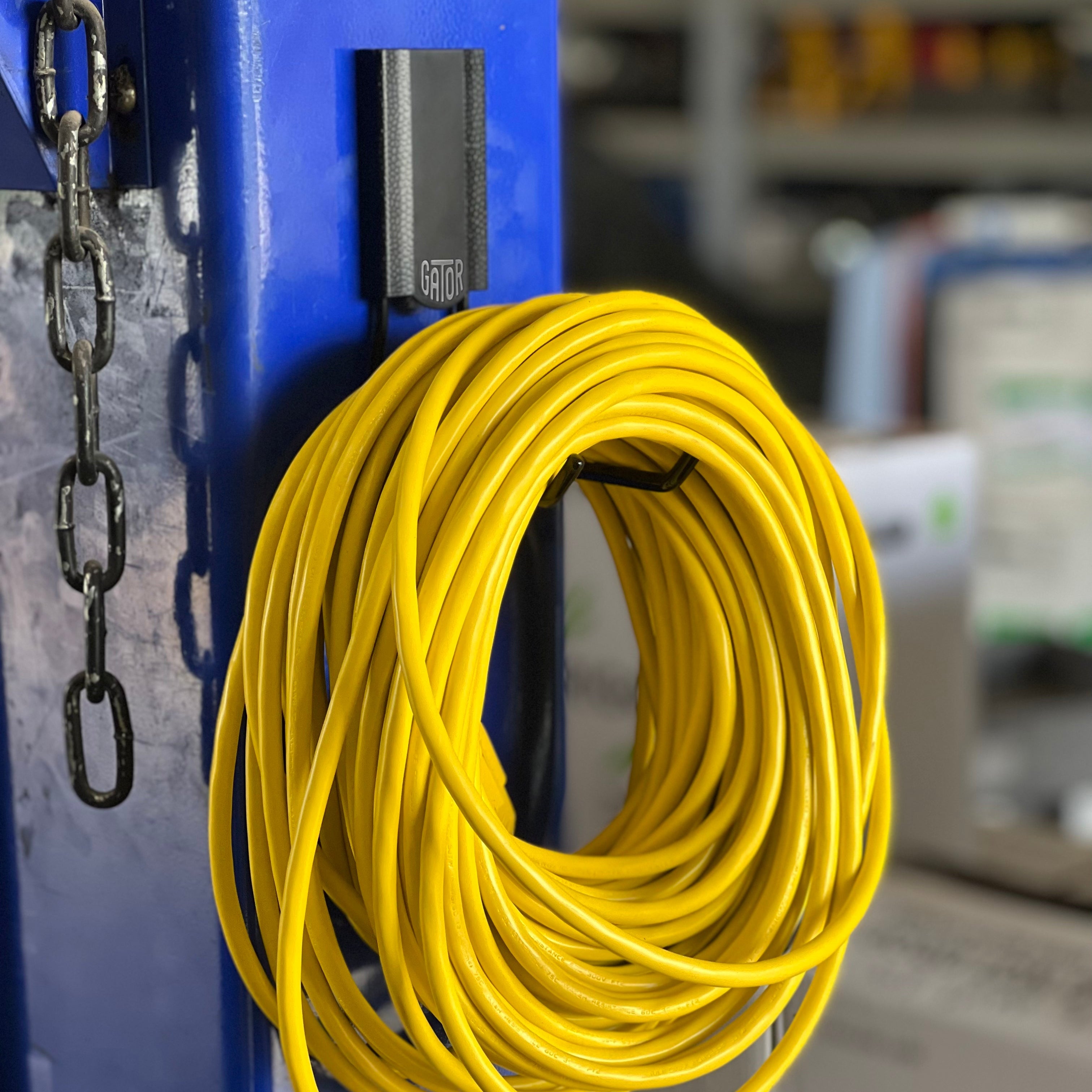 Coiled yellow extension cord hanging from a Gator magnetic hook on a blue steel post.