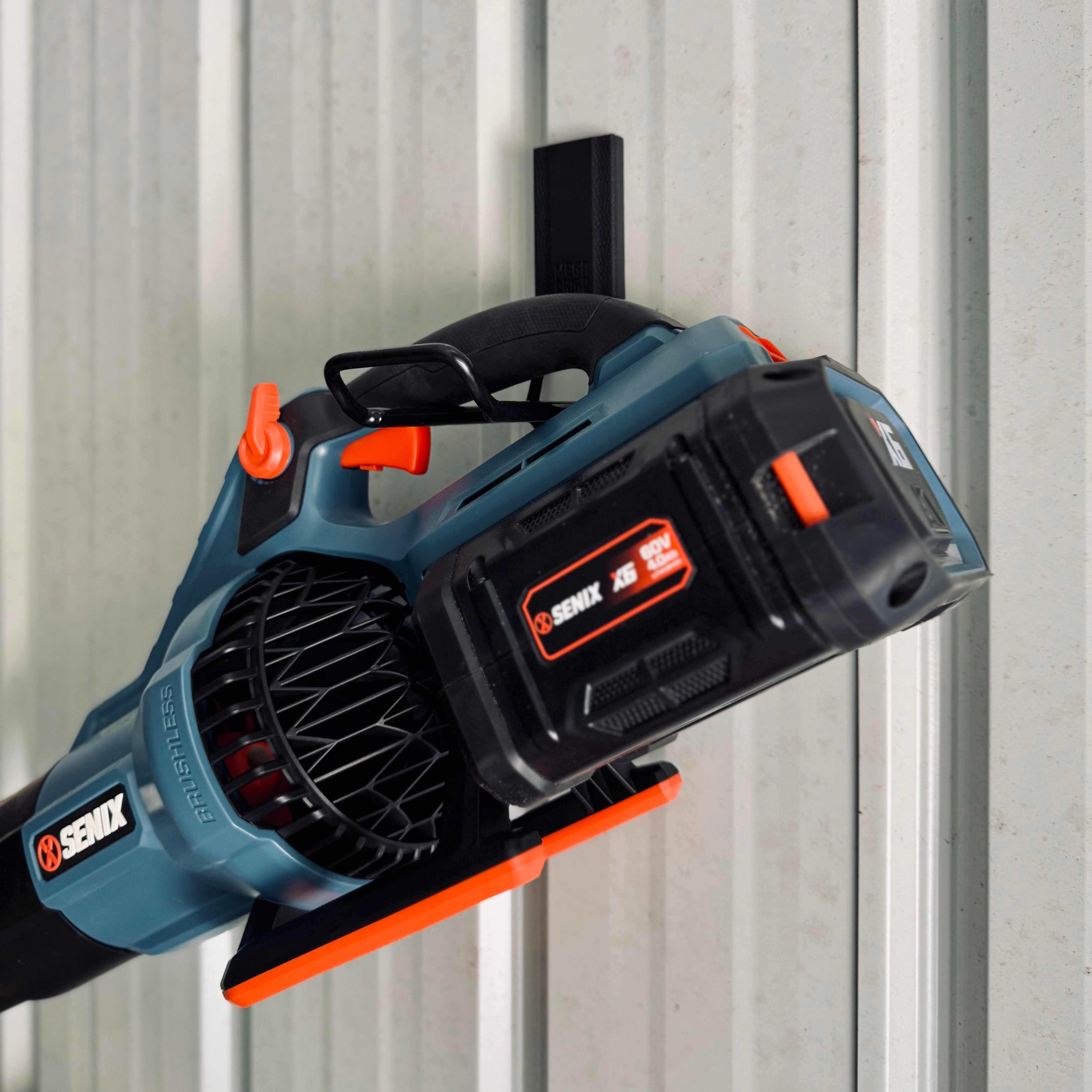 A cordless leaf blower is hanging from a red Gator Magnetics magnetic hook mounted on a steel wall.