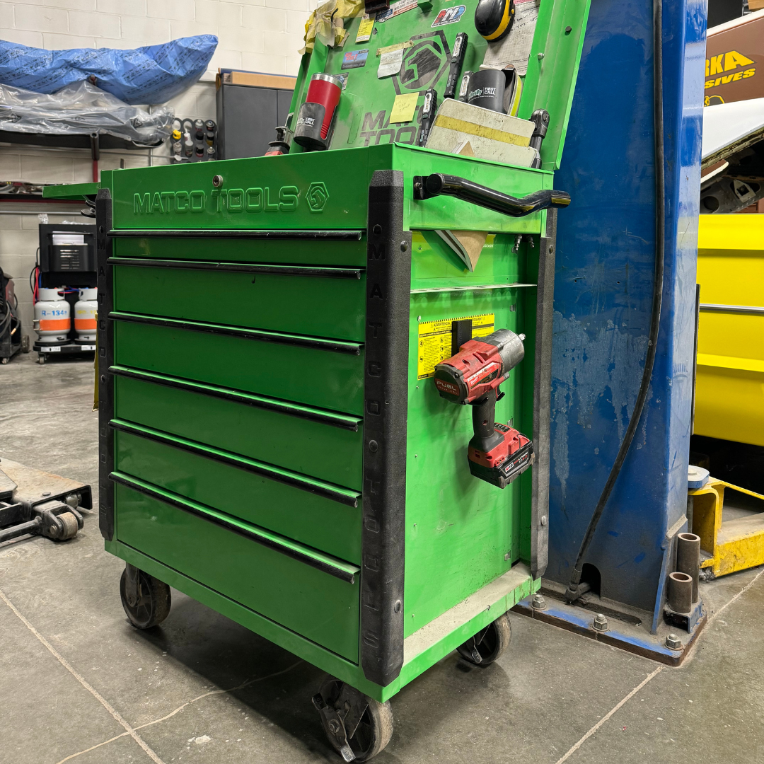 A cordless power drill is stored on a red magnetic hook attached to the green steel side panel of a Matco Tools rolling tool chest.