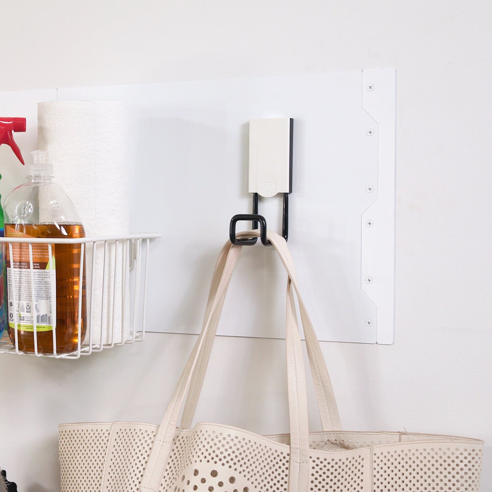 Cream tote bag hanging from a black Gator magnetic hook on a white Gator Steel Wall Panel.