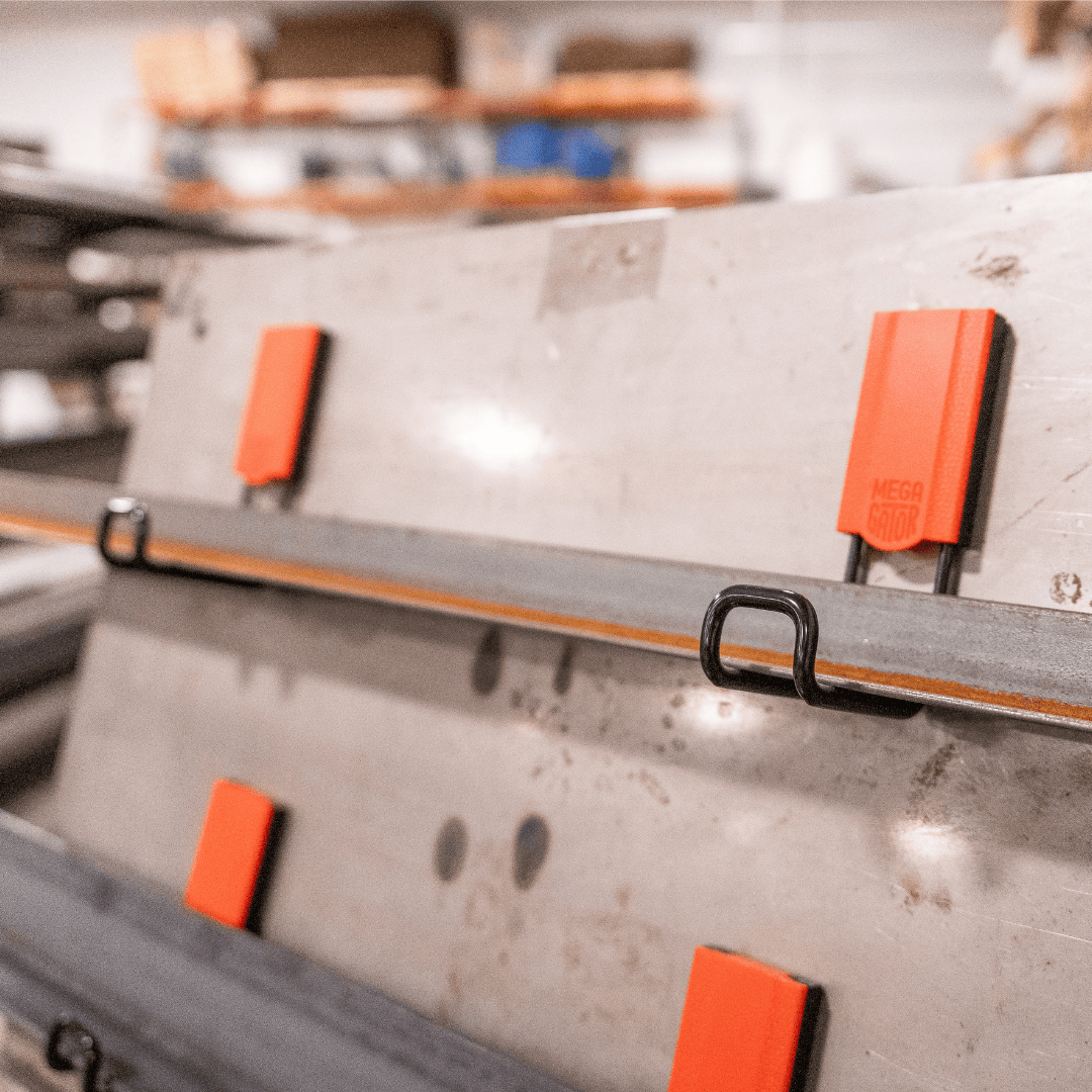 Four red Gator Magnetics magnetic hooks are mounted on a steel workshop wall holding two long metal bars with black hooks.
