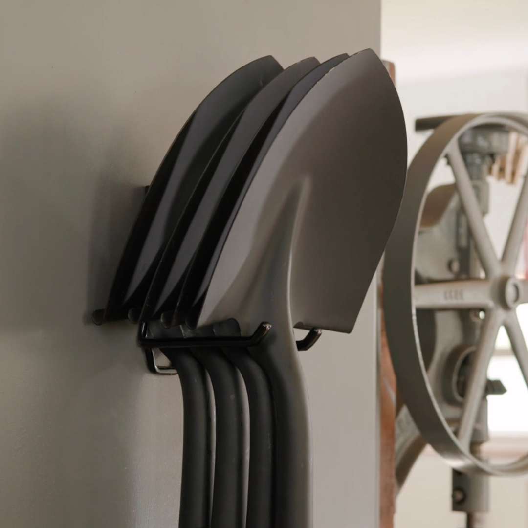 Four shovels hanging from a black Gator magnetic hook on a steel wall panel.