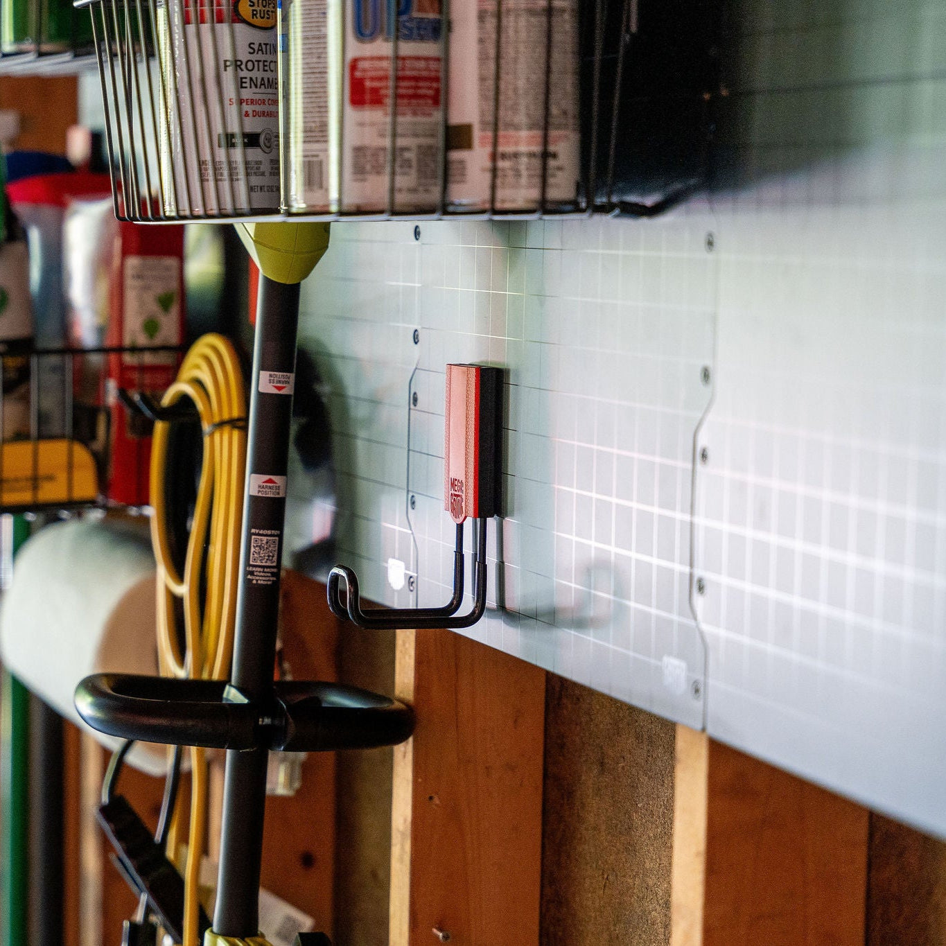 Long-handled garden tool stored on a Gator Magnetics hook attached to a metal grid wall panel in a well-organized garage