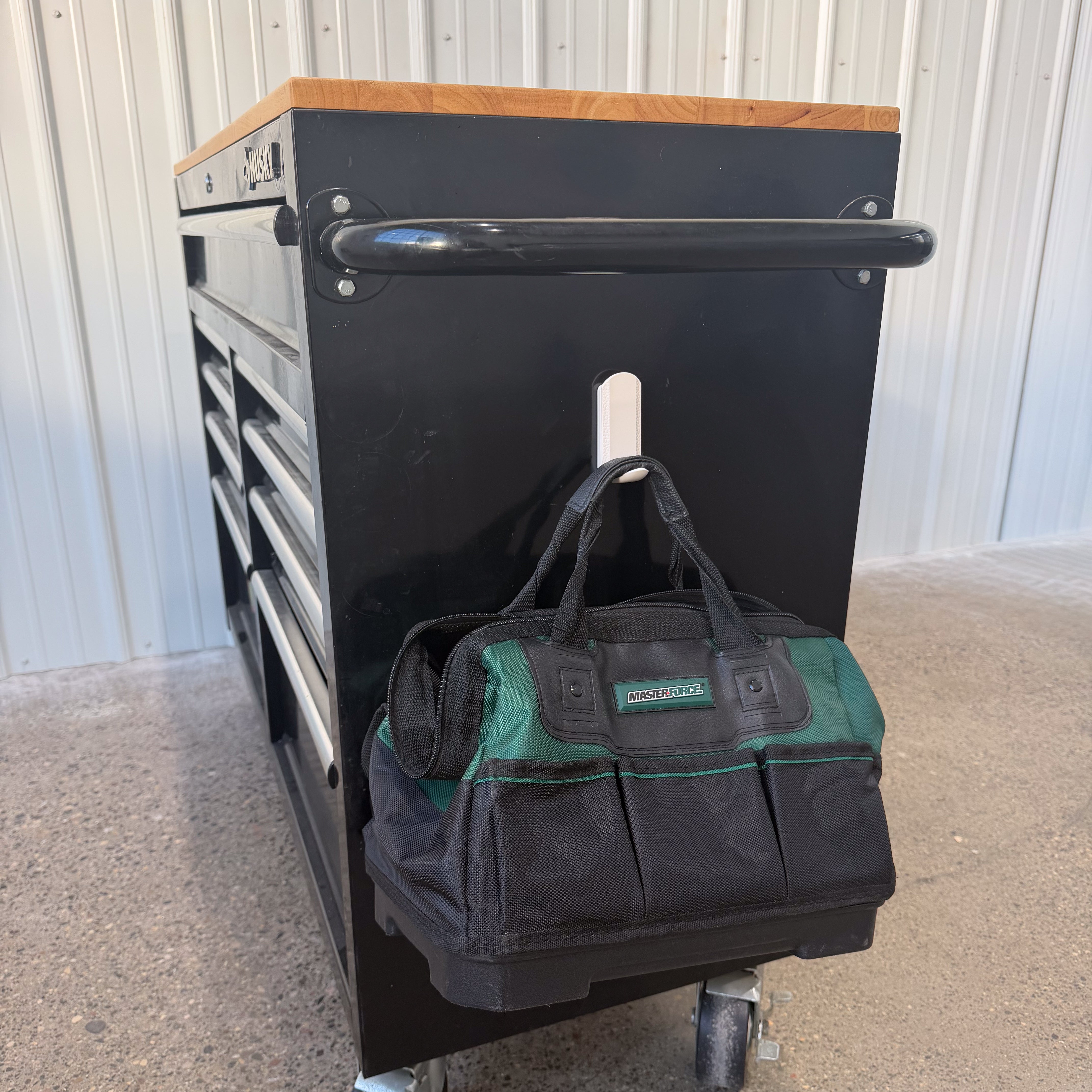 Green and black tool bag hanging from a white Gator magnetic hook on a black steel tool chest.