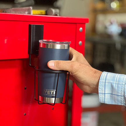 A hand places a blue YETI tumbler into a black Gator Magnetics magnetic cup holder on a red steel toolbox.