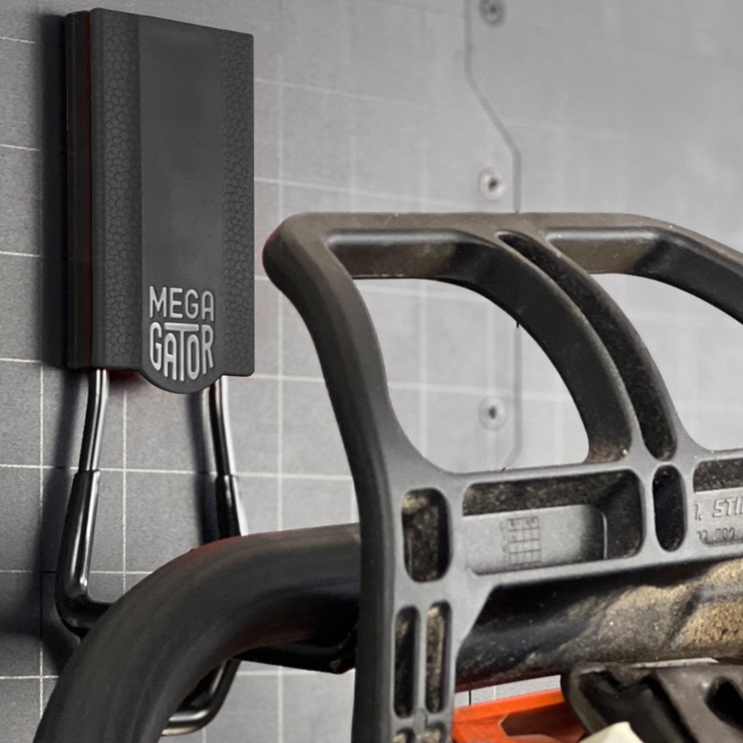 Gator heavy-duty magnetic hook holds a chainsaw handle on a black grid-patterned steel wall panel.