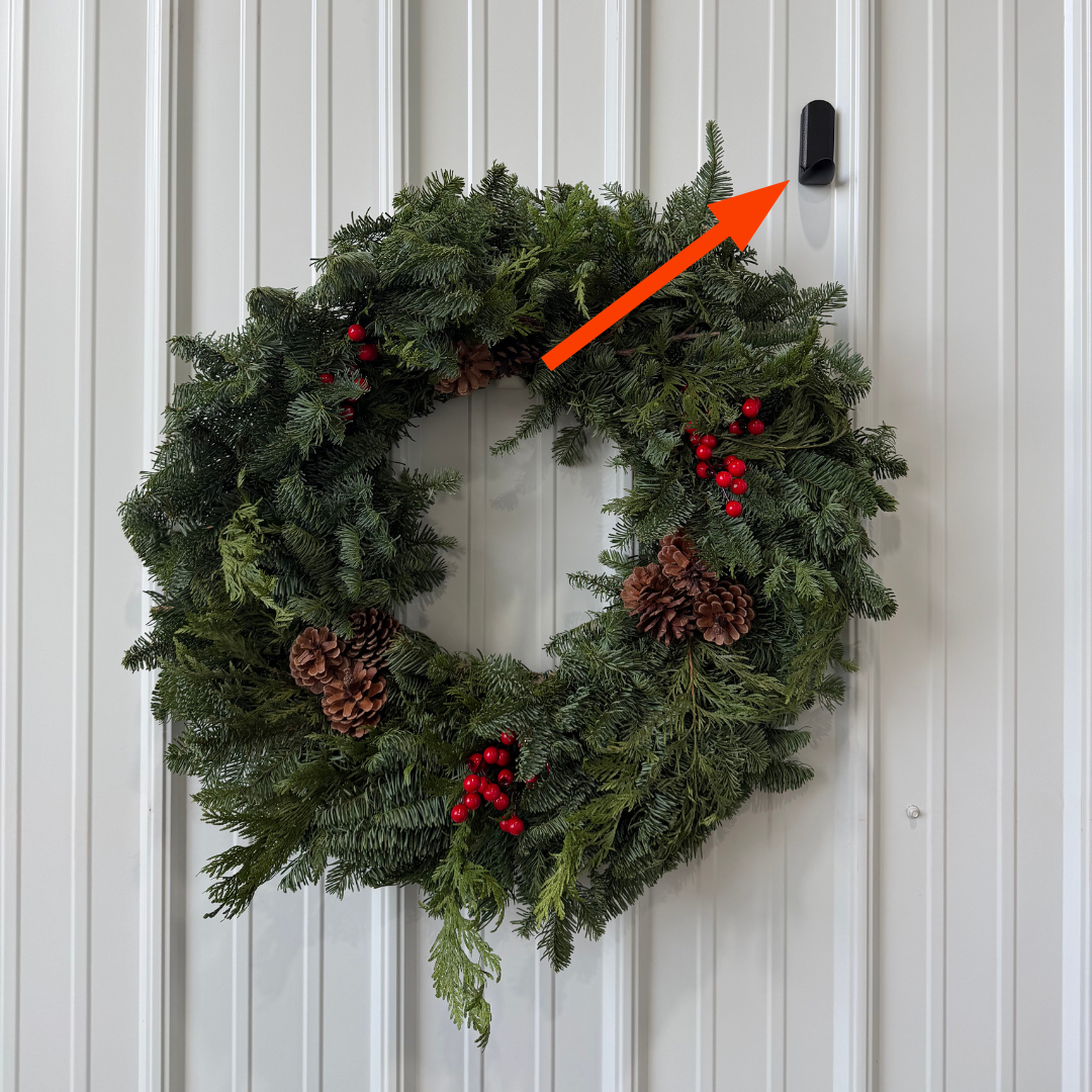 A holiday wreath is hung on a white steel wall using a black Gator Magnetics magnetic hook.