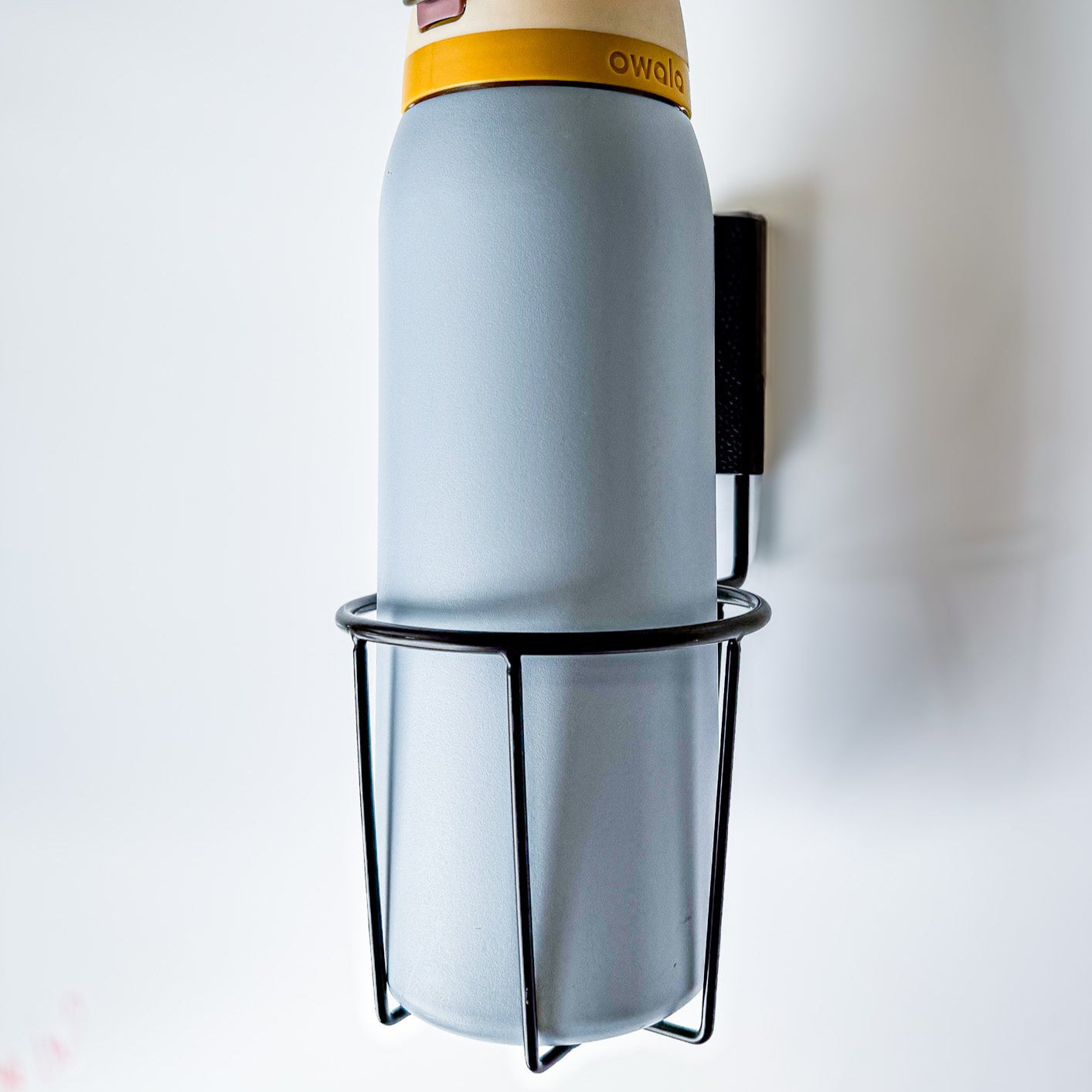 Insulated water bottle secured in a black Gator magnetic cup holder on a white steel wall panel.
