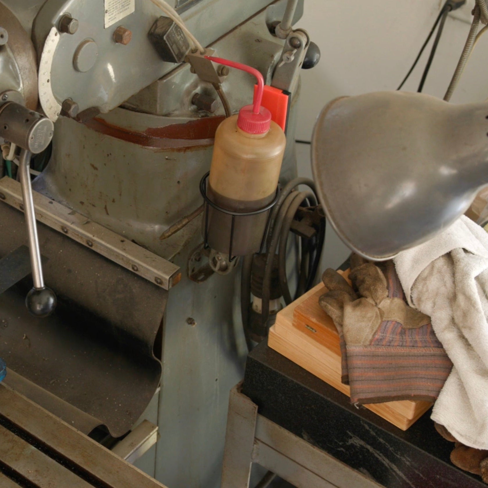 A Gator Magnetics magnetic cup holder holds a plastic lubrication bottle on the steel surface of a vintage metal lathe.