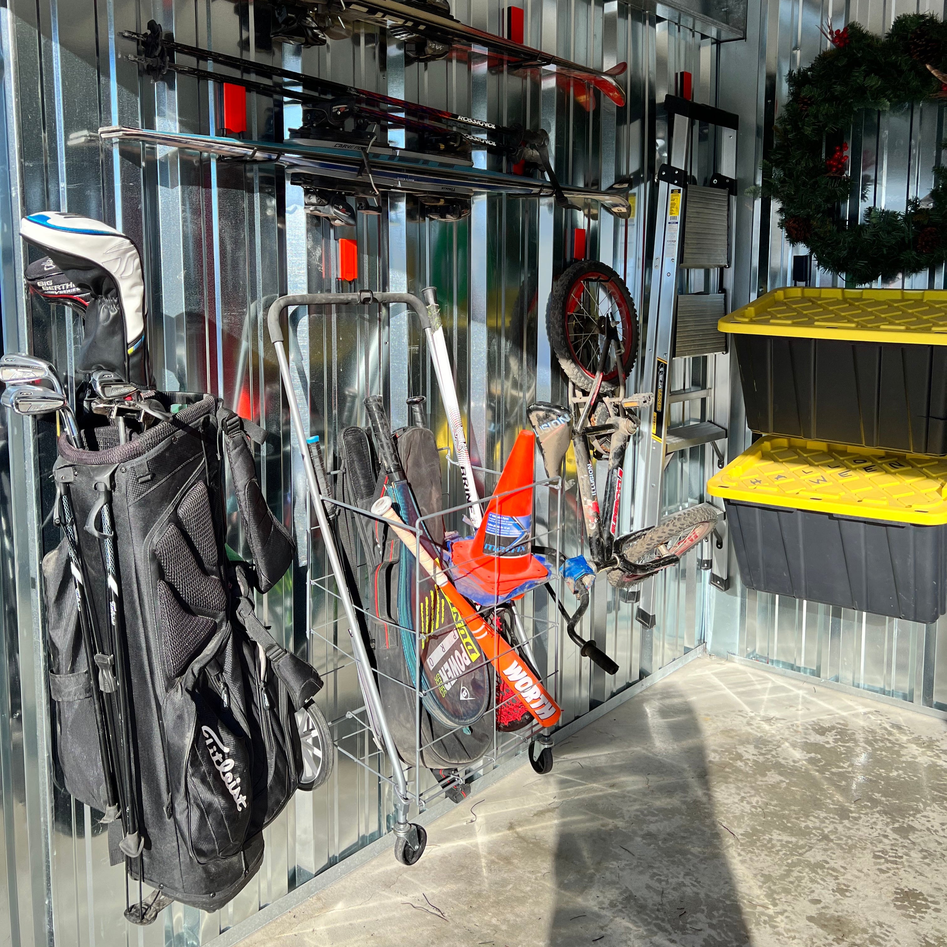 Gator magnetic hooks and basket organize a golf bag, baseball bats and sports gear on a steel wall panel.
