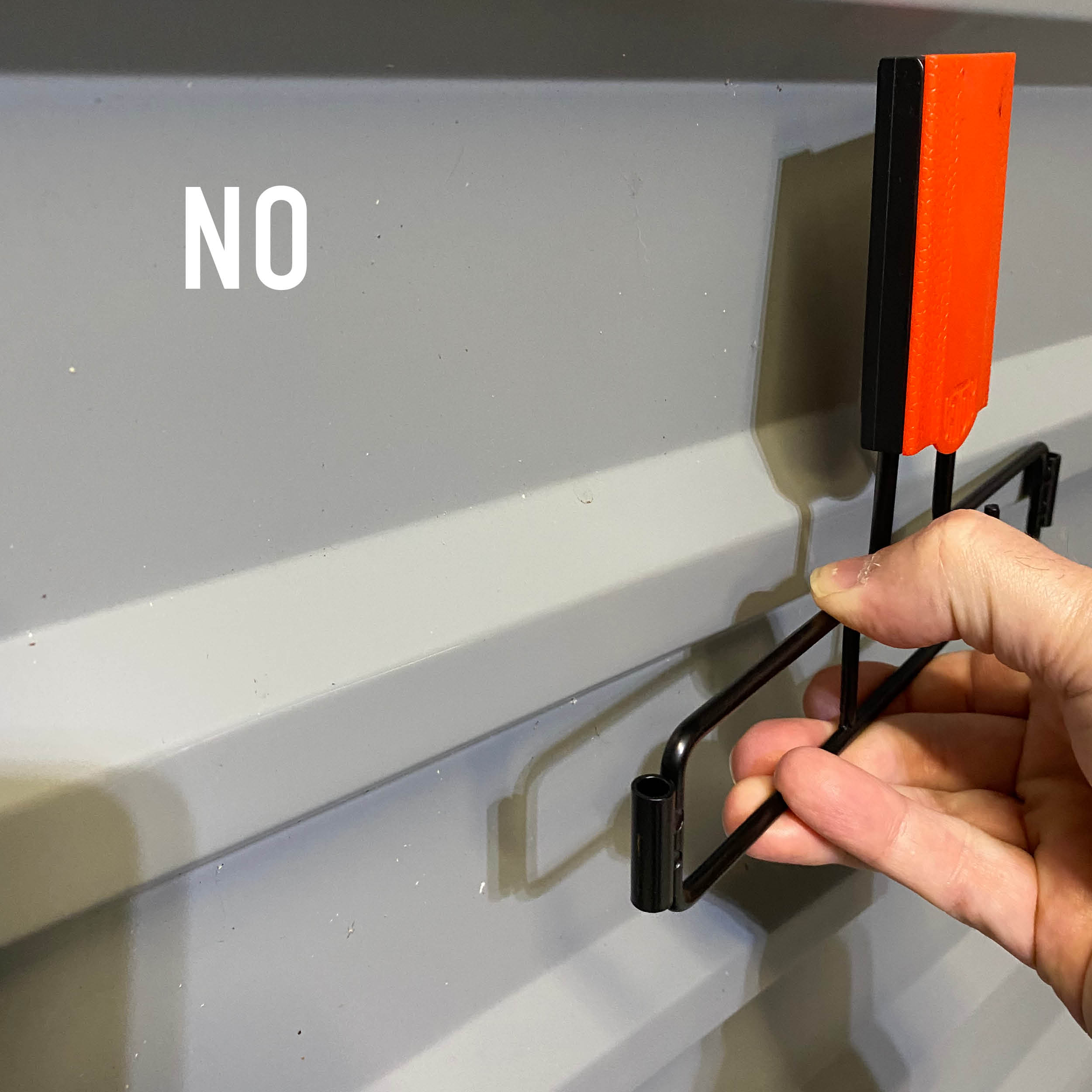 A person's hand is shown trying to attach a Gator Magnetics black and red magnetic hook onto a textured steel wall panel.