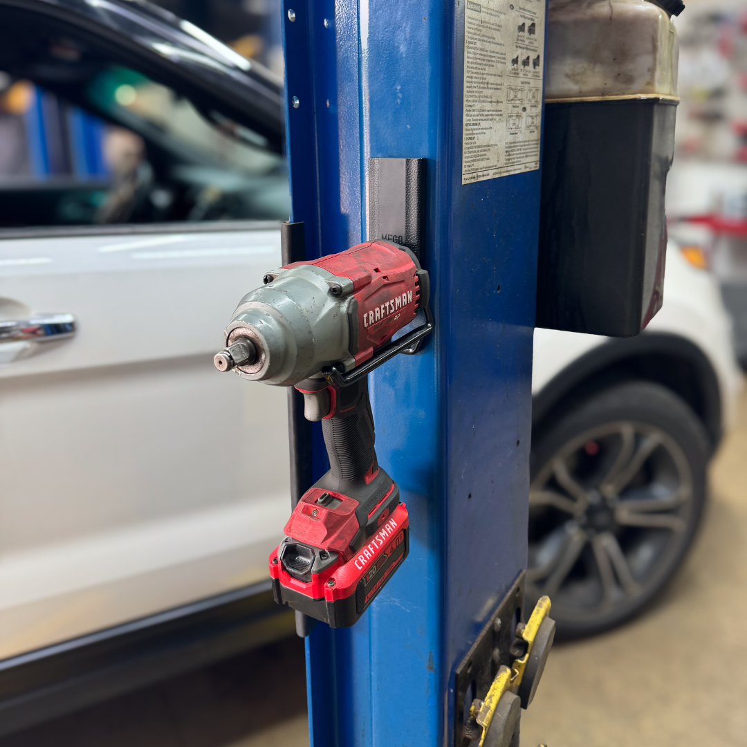 A red and gray Craftsman cordless impact driver is held on a blue steel post using a black Gator Magnetics hook.