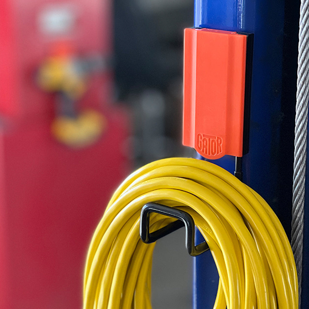 A Gator Magnetics red magnetic hook is mounted on a blue steel pole holding a coiled yellow extension cord.