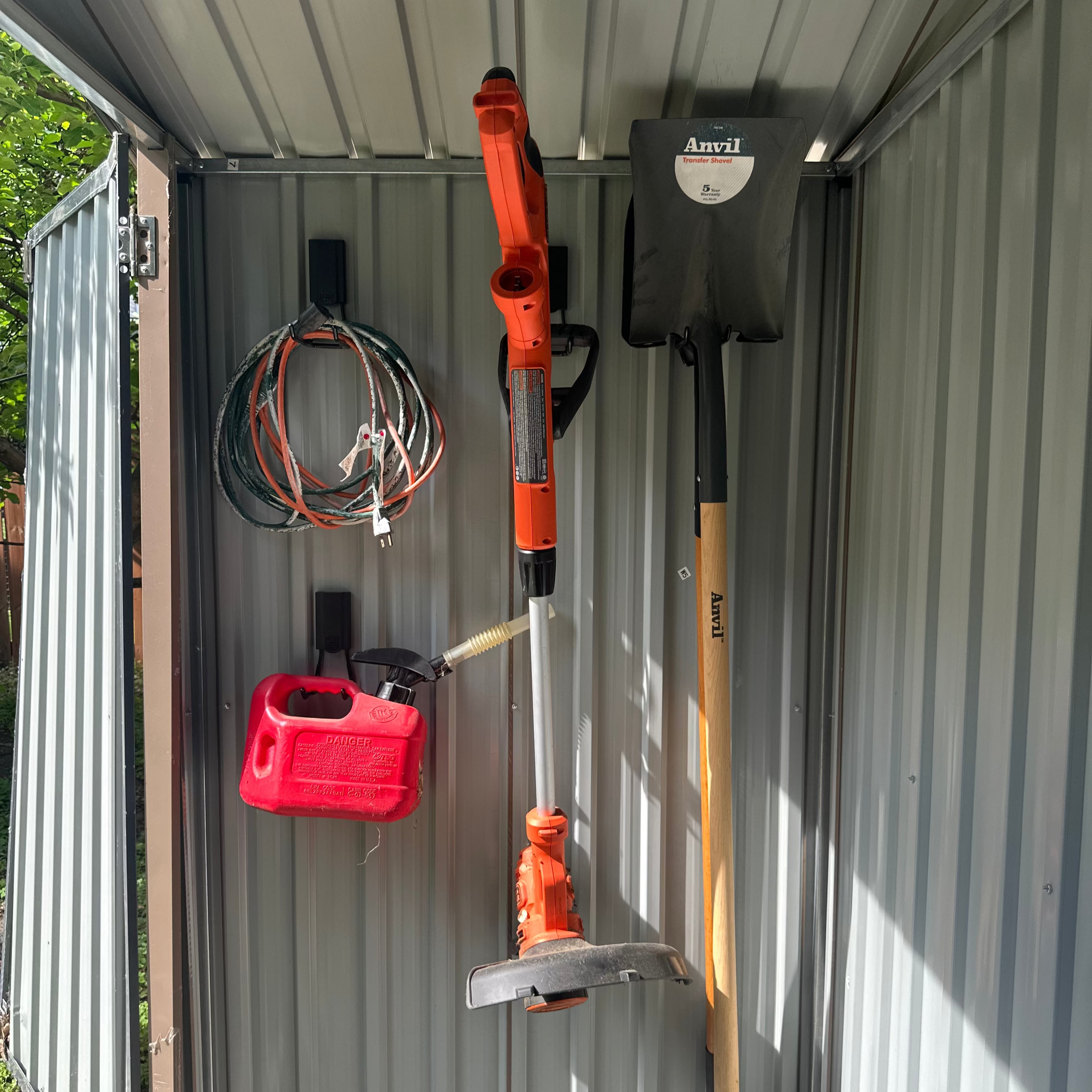 Red Gator magnetic hooks organize a cord, fuel can, weed trimmer and shovel on a galvanized steel shed wall.