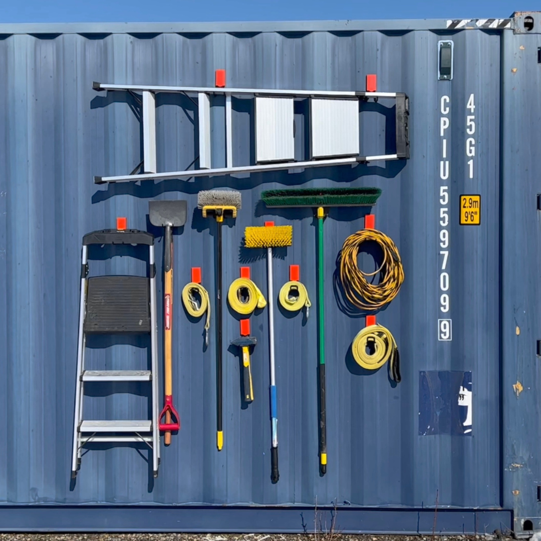 Red Gator magnetic hooks organize ladder, shovel, brushes and cords on a blue steel shipping container.