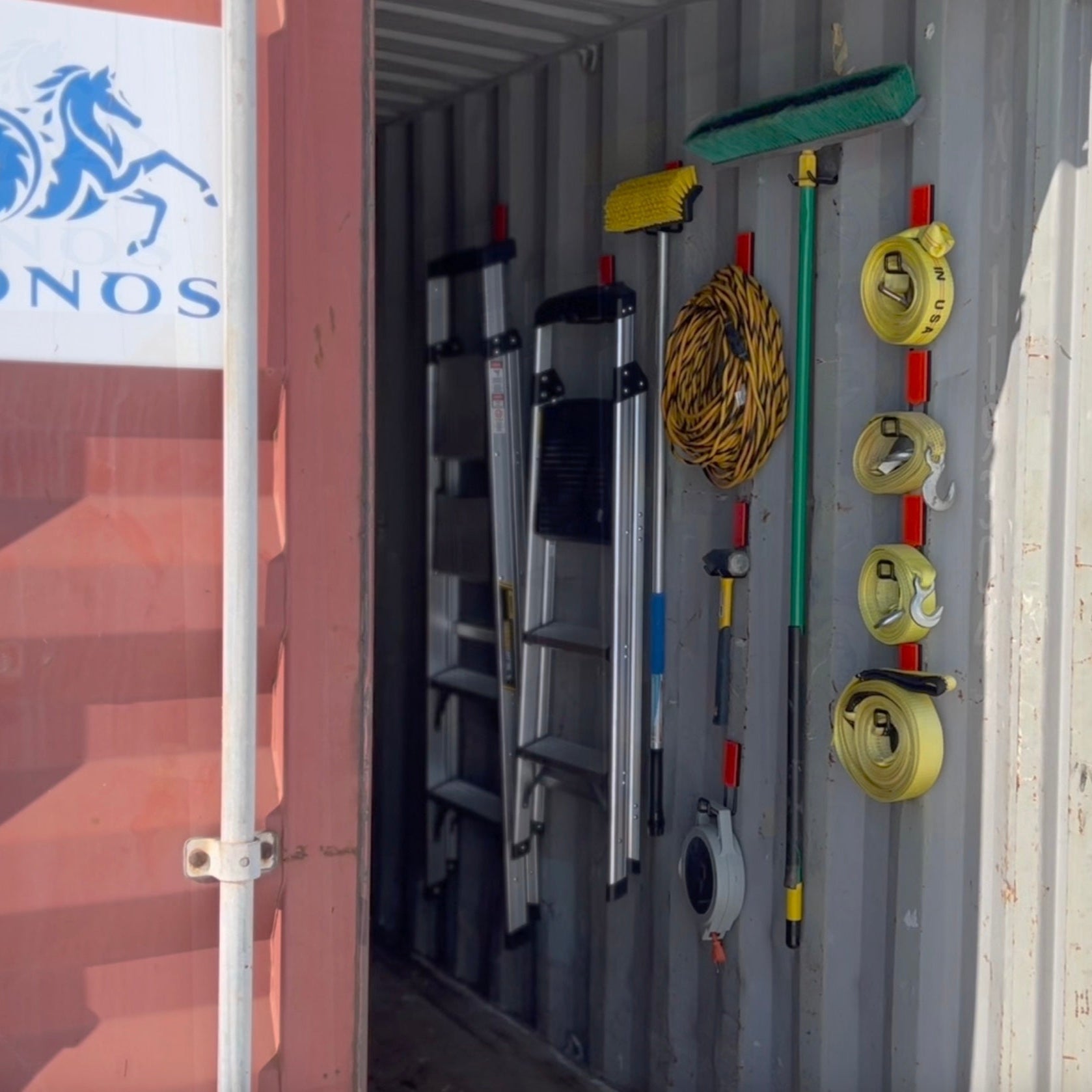 Red Gator magnetic hooks organize ladders, extension cords, broom, hammer and ratchet straps on a steel wall.