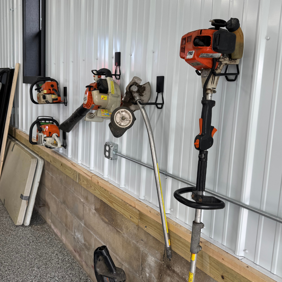 Red Gator magnetic hooks organize two chainsaws and a leaf blower on a steel wall.