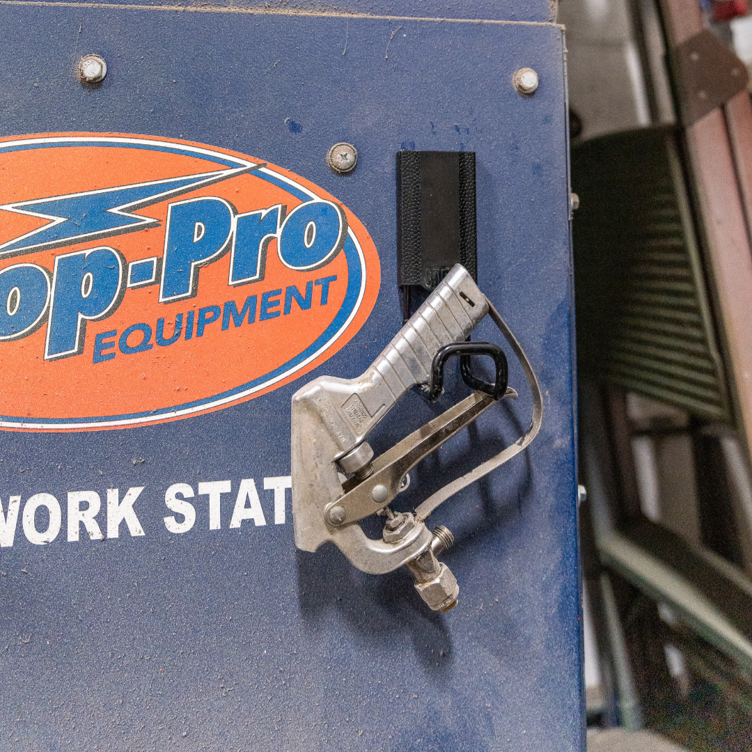 A silver blow gun nozzle is hung by a black magnetic hook from Gator Magnetics on the steel door of a blue Top-Pro Equipment workstation.