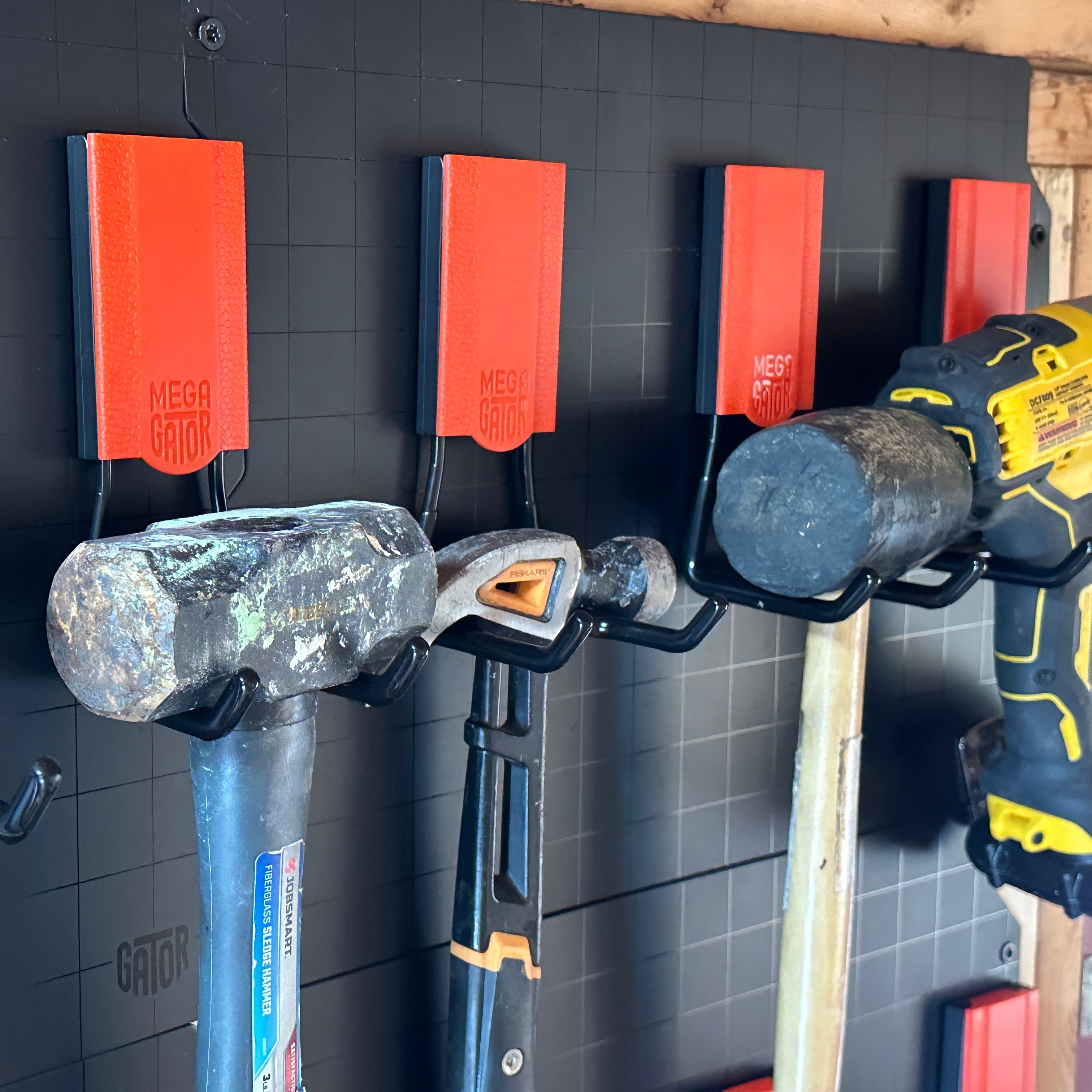 Sledgehammer, claw hammer and mallet hanging from red Gator hooks on a black steel wall panel.
