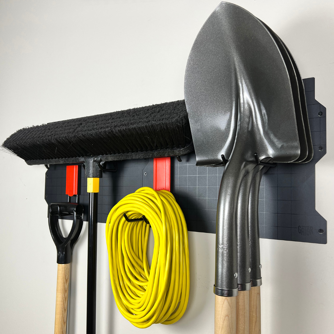 Gator Steel Wall Panel with red magnetic hooks holding three shovels, a broom and extension cord.