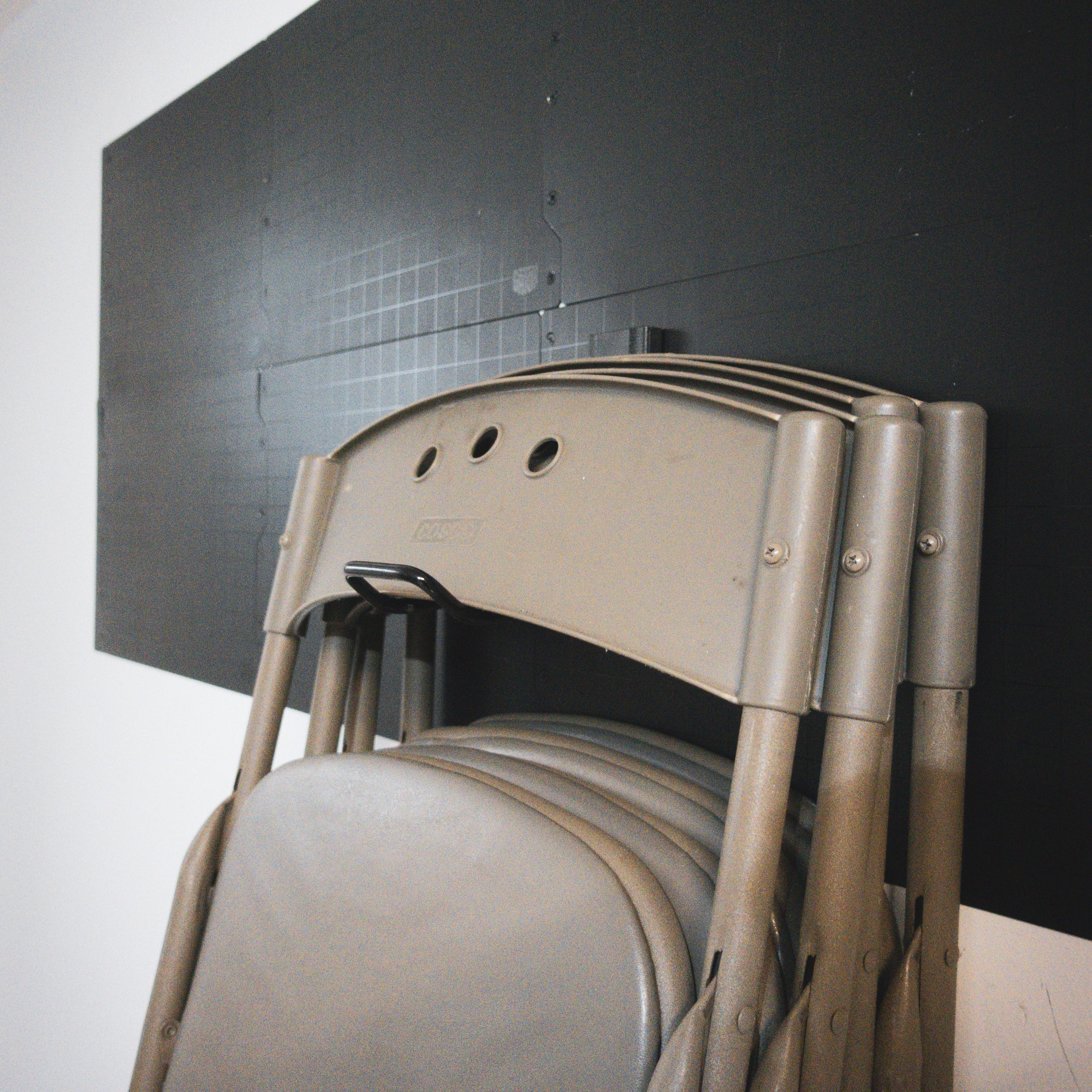 Tan folding chairs hanging from a black Gator magnetic hook on a black steel wall panel.