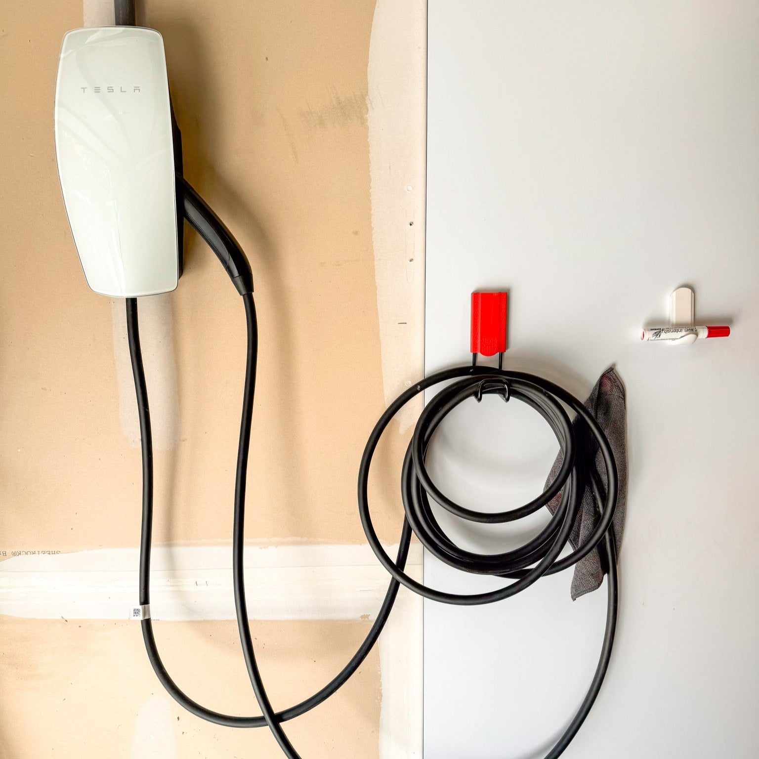 Tesla wall charger installed in a garage with its charging cable neatly organized using a Gator Magnetics hook on a metal cabinet