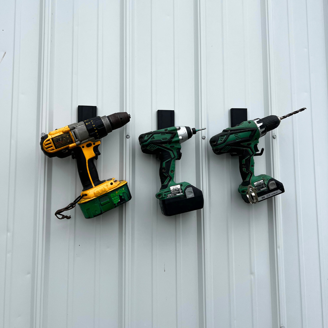 Three cordless drills hanging from black Gator magnetic hooks on a vertical steel wall panel.