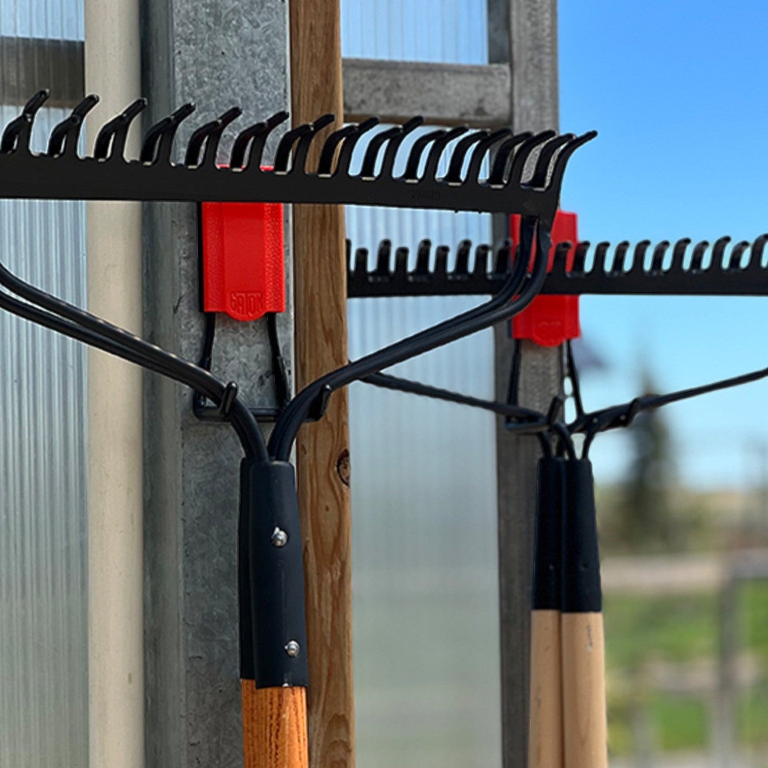 Two leaf rakes hang from red Gator magnetic hooks on a galvanized steel wall.