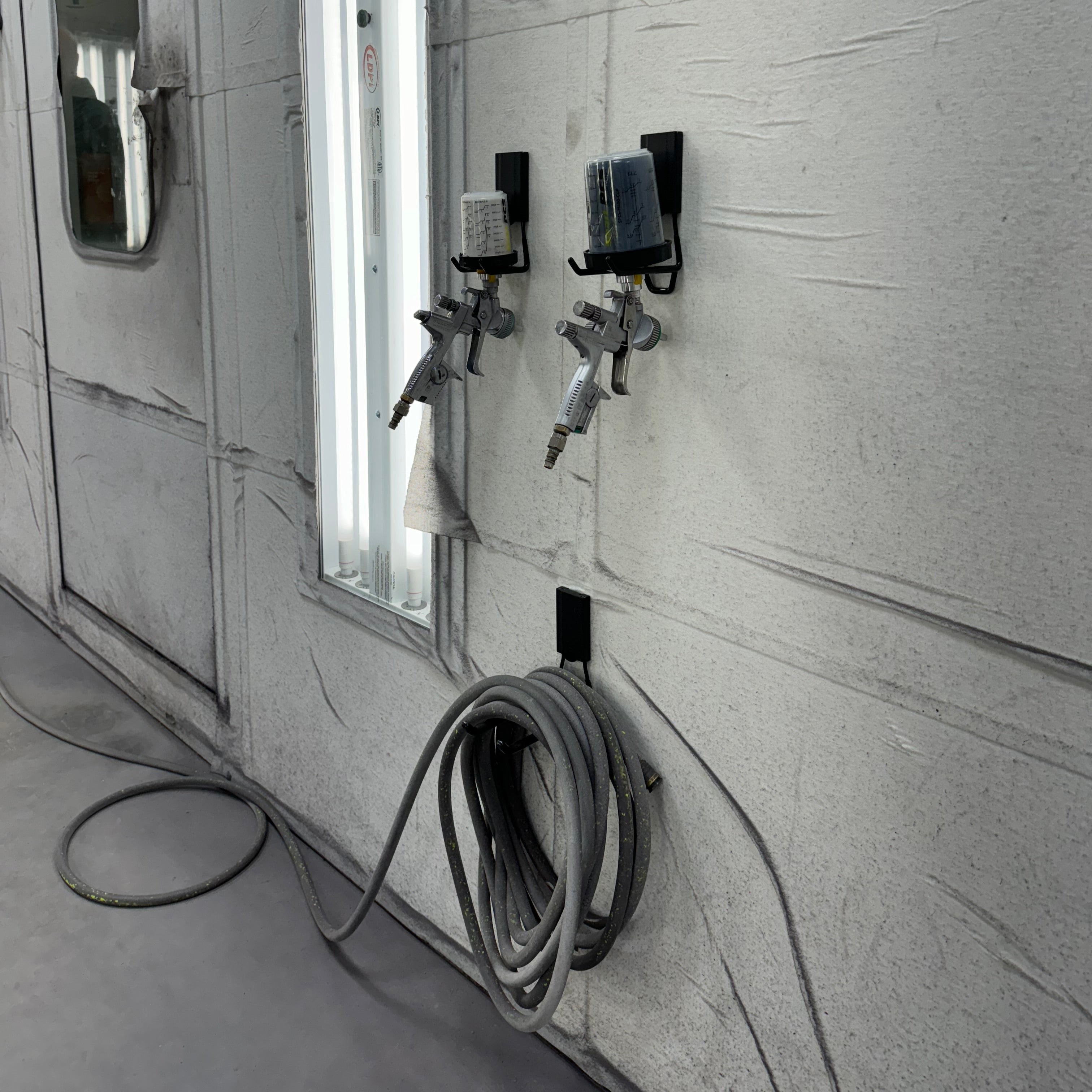 Two paint spray guns and a coiled air hose stored on black magnetic hooks on a steel wall.