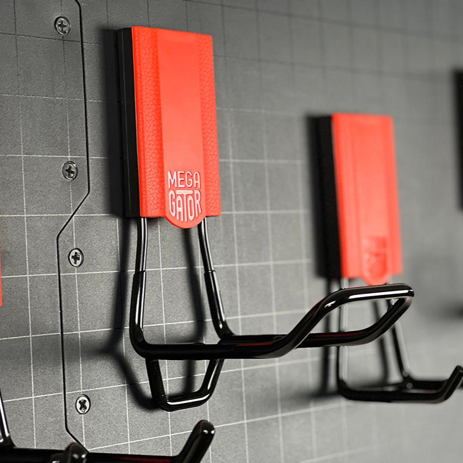 Two red Gator magnetic hooks hold coiled black extension cords on a grid-patterned steel wall panel.