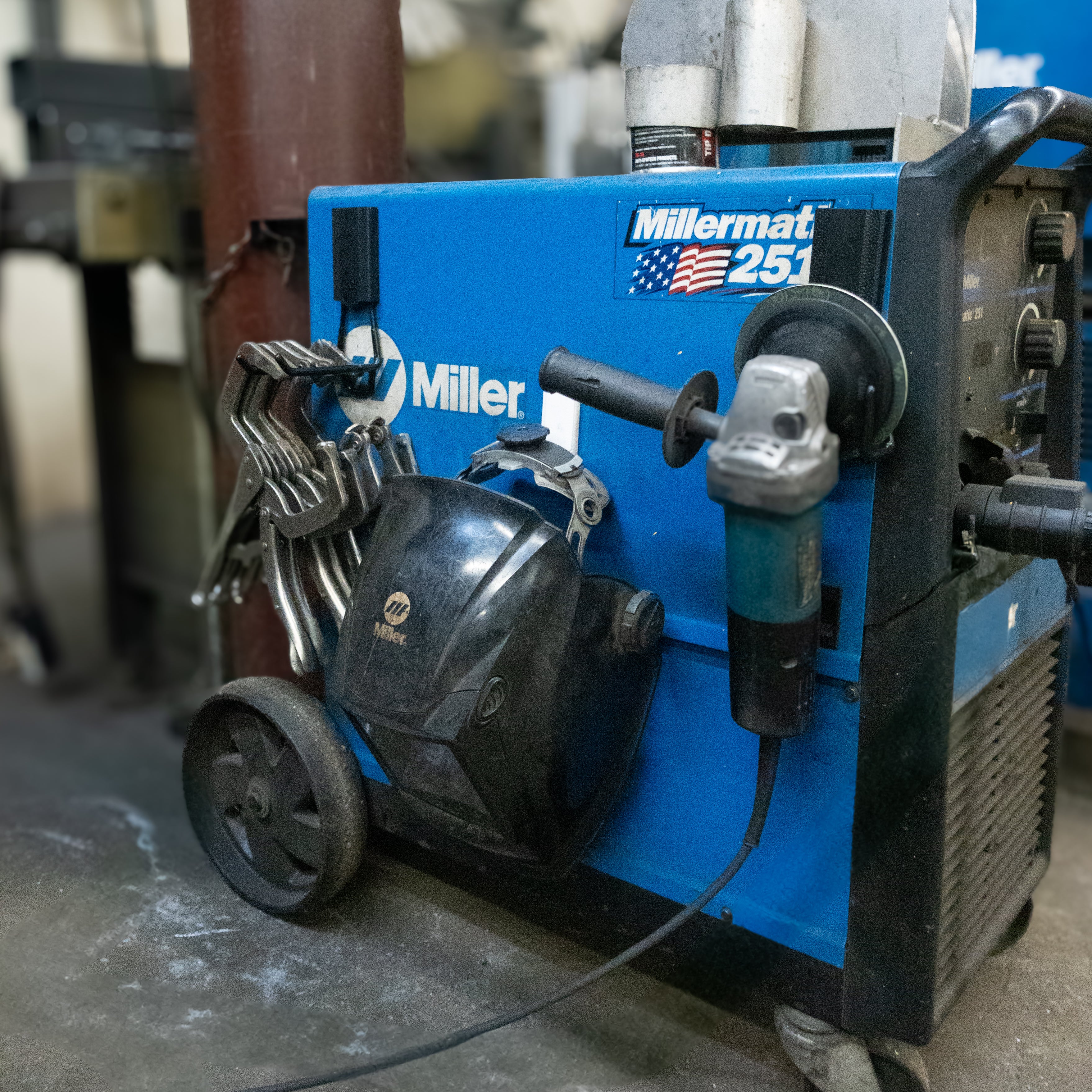 Two red Gator magnetic hooks hold a welding mask and angle grinder on a Miller welding machine.