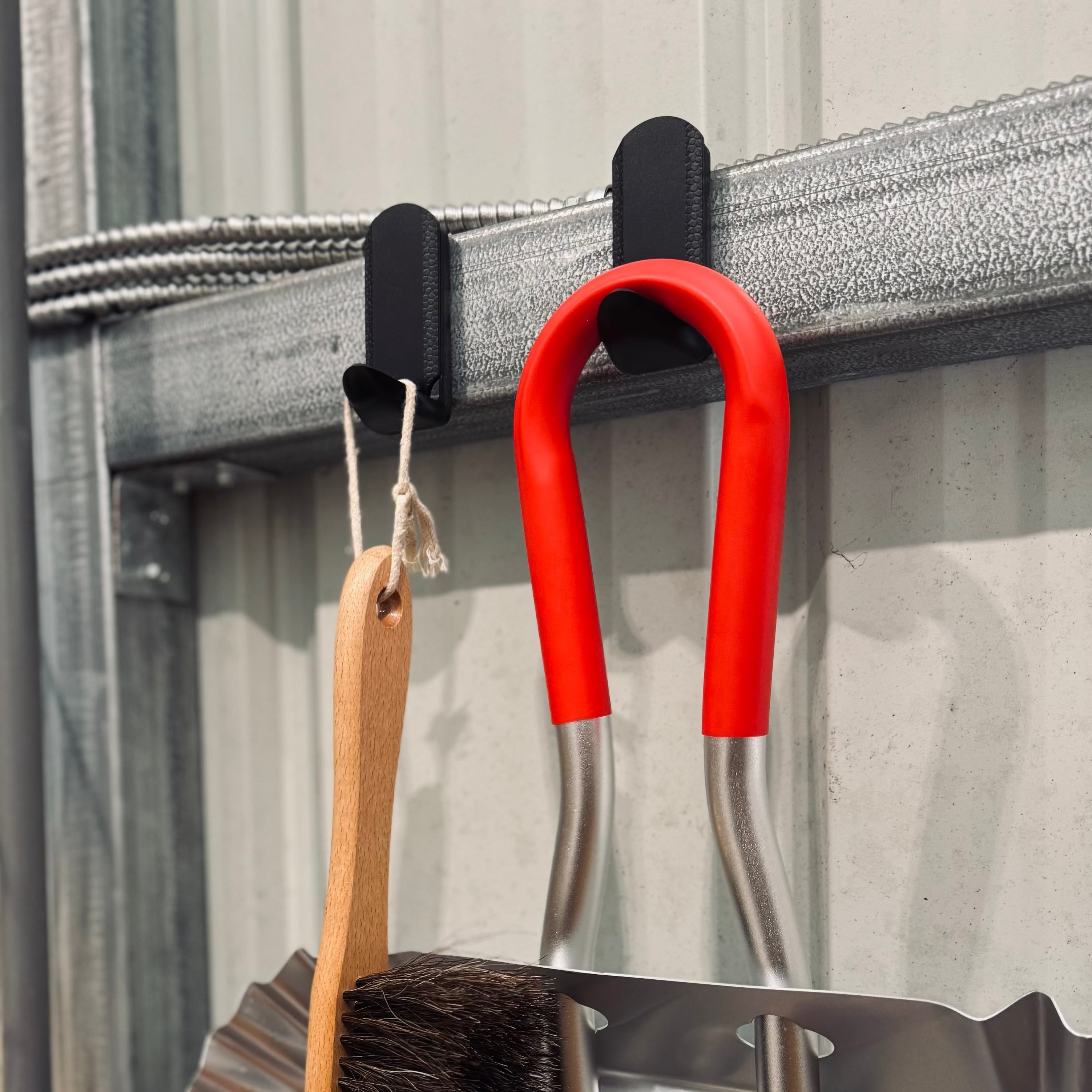 Two red Gator MINI magnetic hooks hold a paintbrush and hand tool on a corrugated steel wall.