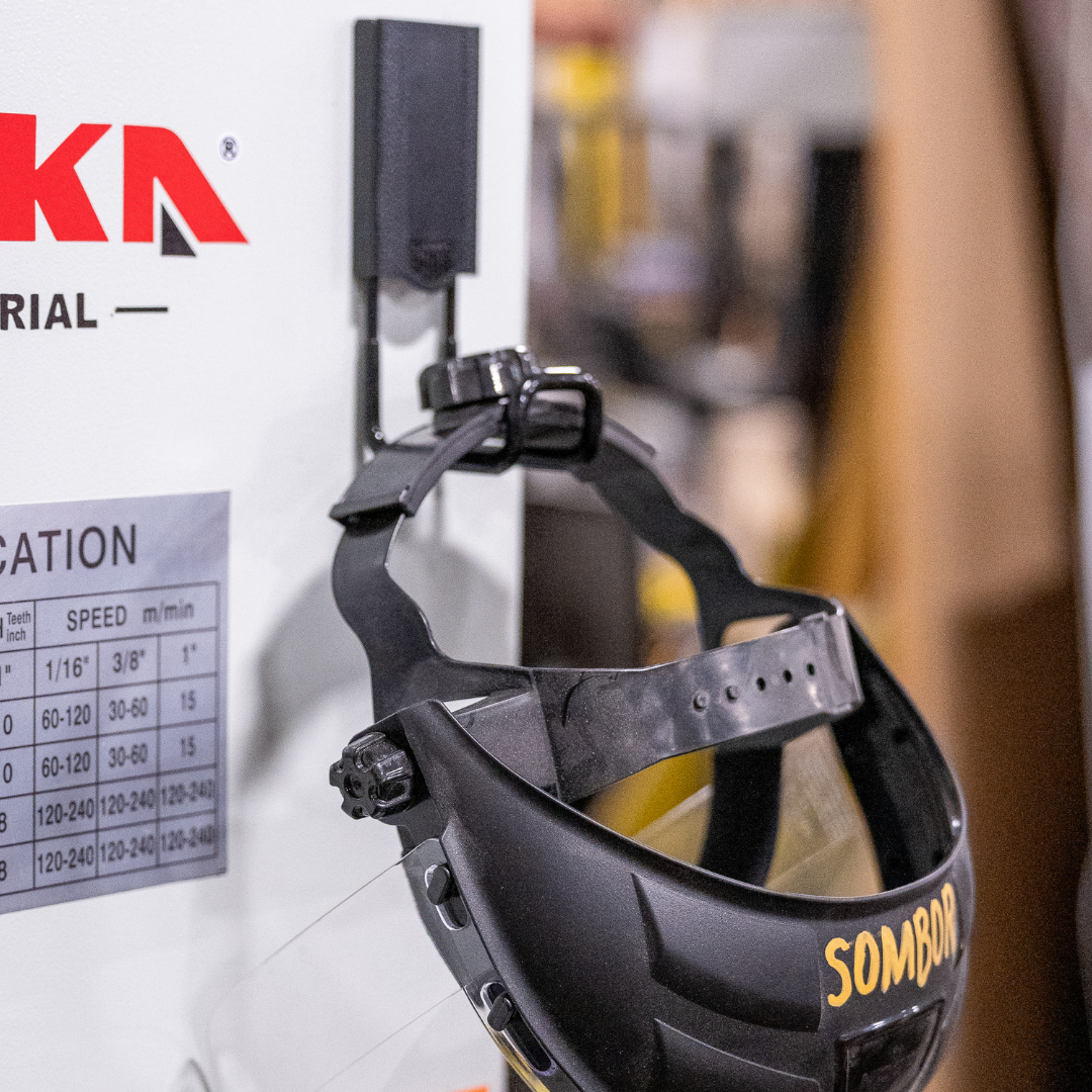 Welding helmet hanging from a red Gator magnetic hook on a white steel equipment panel.