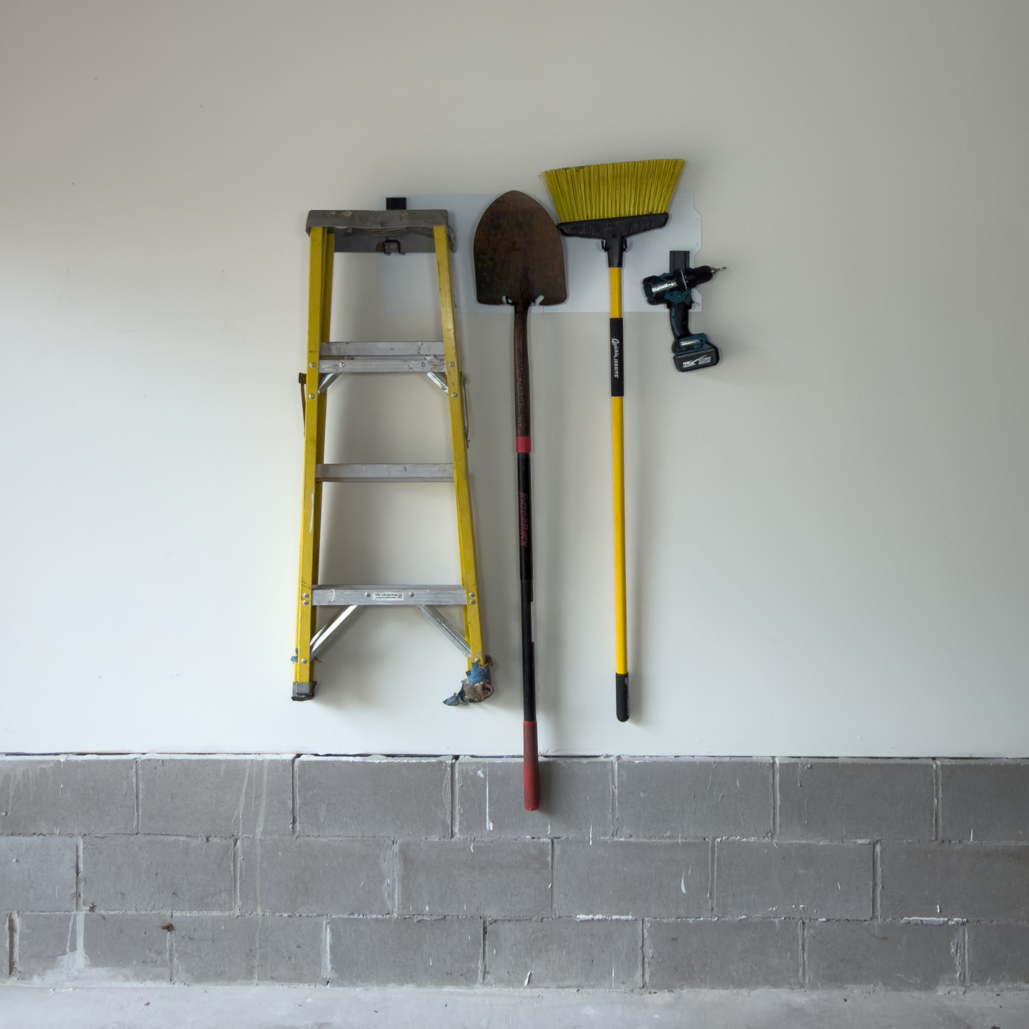 White 34-inch magnetic wall storage system holding a ladder, broom, shovel and drill.