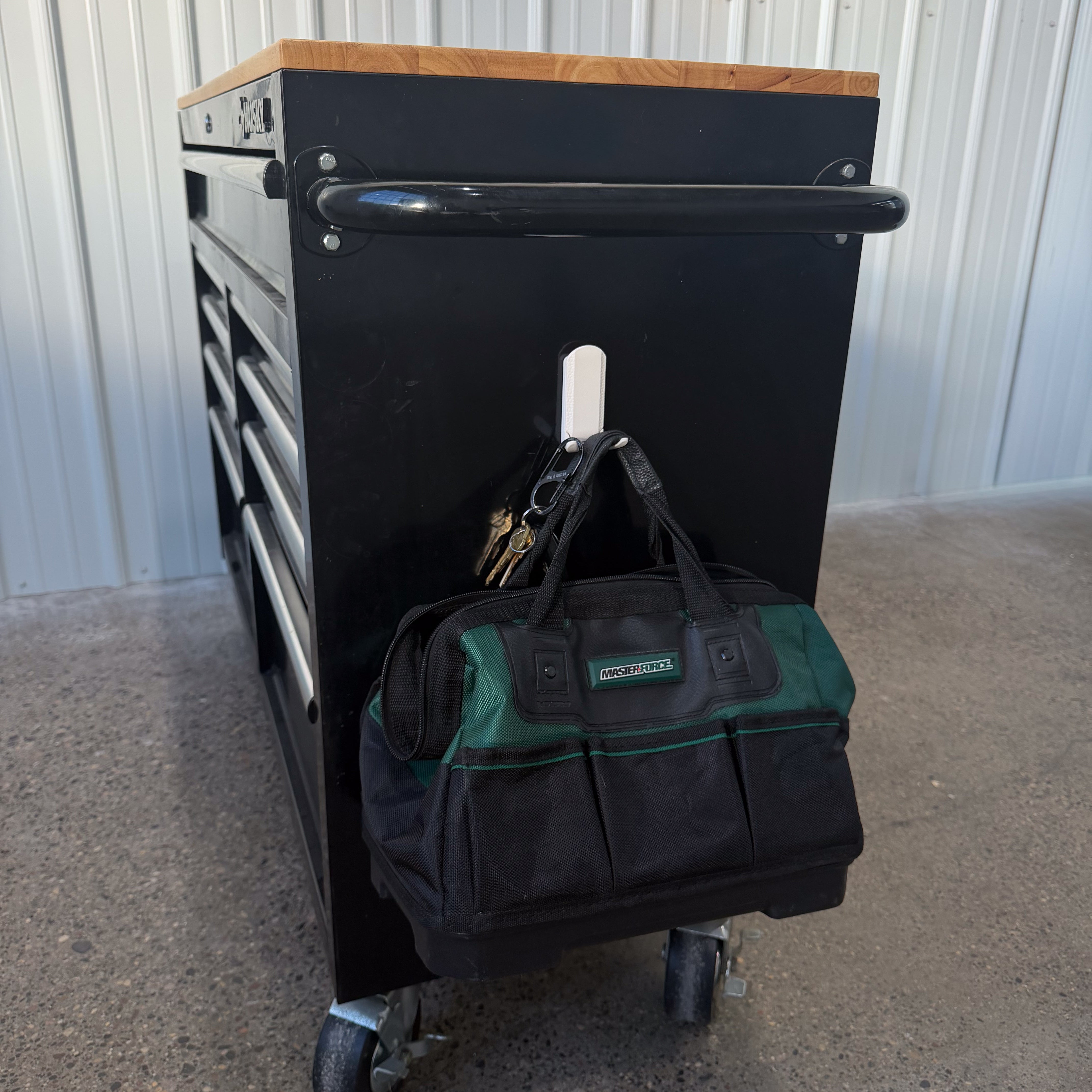 White Gator Dual Prong MINI magnetic hook holds a tool bag and keys on a black steel panel.