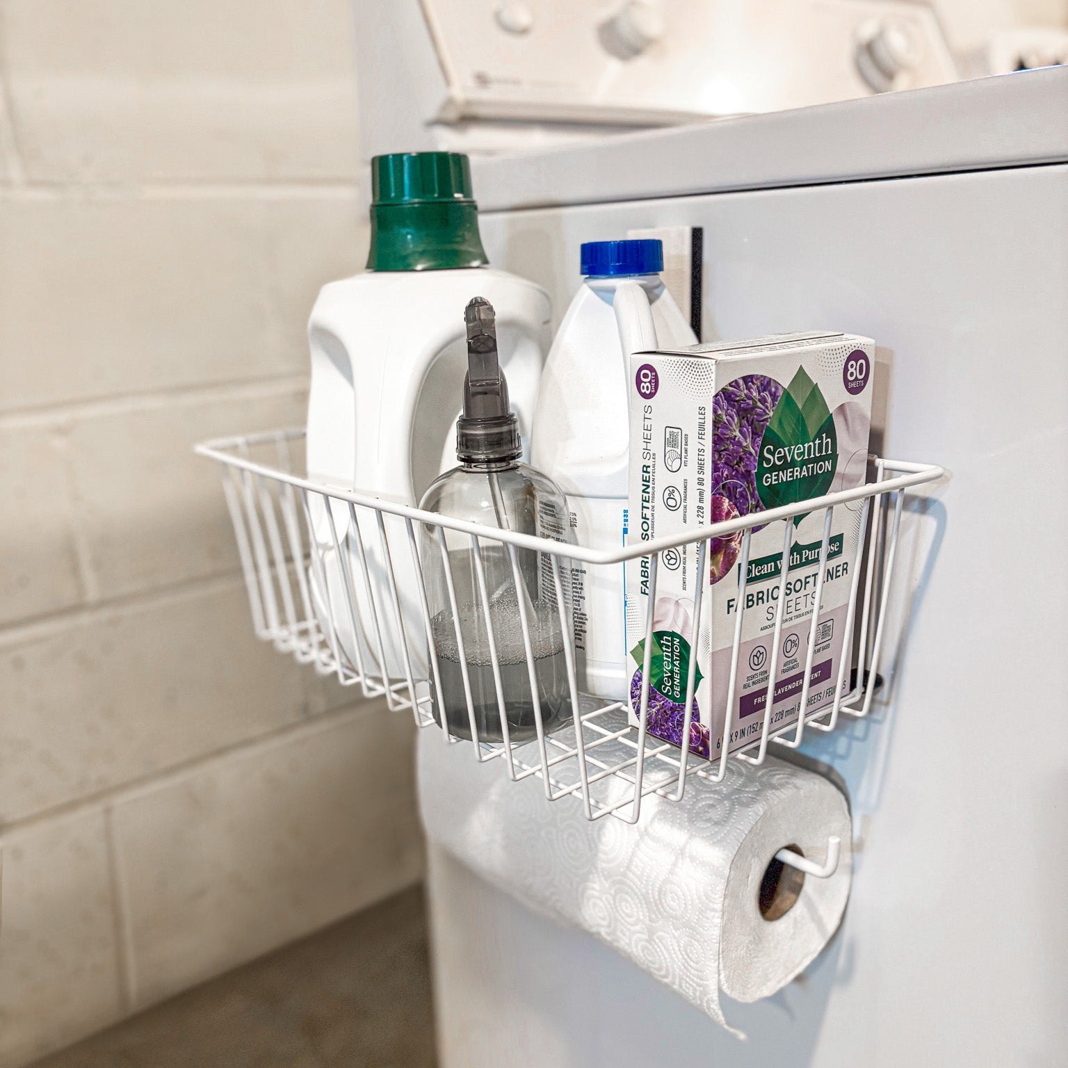 A white magnetic storage basket from Gator Magnetics holds laundry detergent, fabric softener, spray bottle, and fabric softener sheets.
