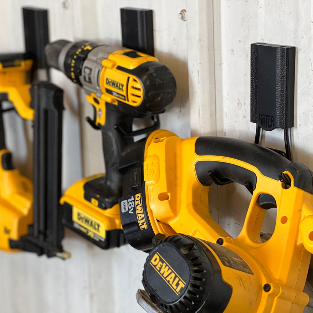 Yellow drill and jigsaw hanging from red Gator magnetic hooks on a white steel wall panel.