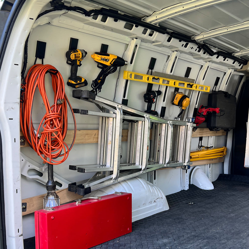 Magnetic hooks securing ladders, power tools, extension cords, and levels inside a work van for efficient mobile tool organization.