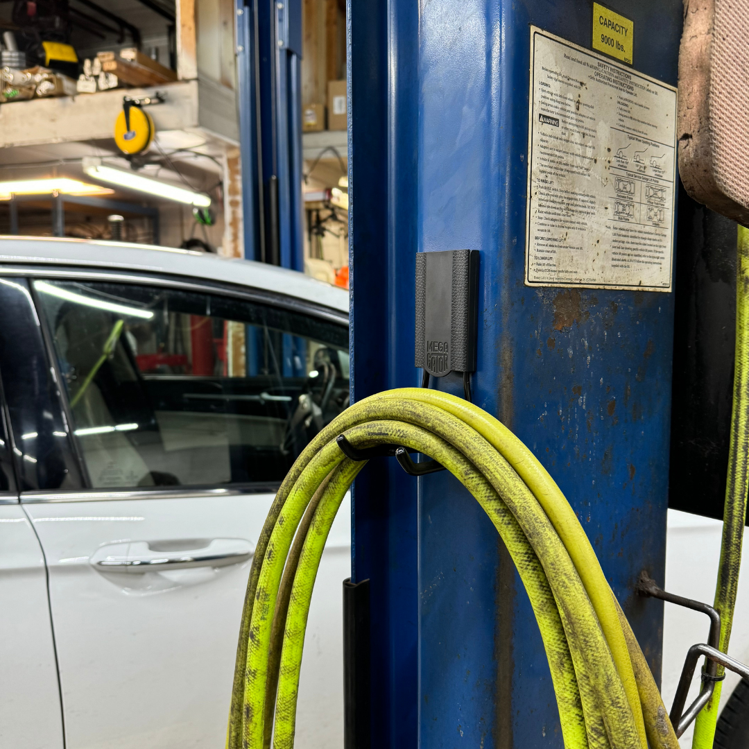Yellow hose looped and hanging on a Mega Gator magnetic hook attached to a blue metal lift post in an auto shop
